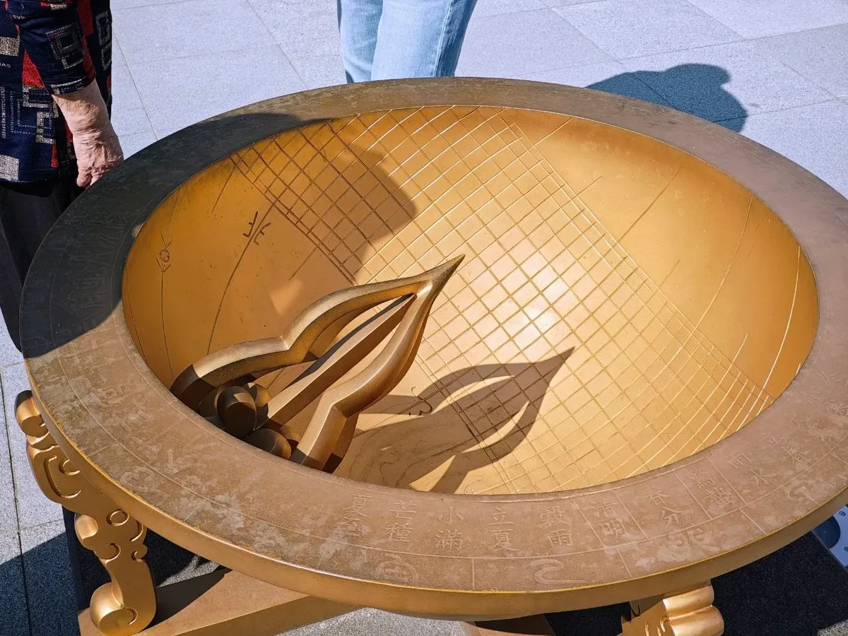 A golden copy of the Joseon hemispherical sundial: a bowl-shaped dial with a grid of hour and season lines, a pointed gnomon casting a shadow, and Chinese characters for the solar terms such as 夏至, 芒種, 小滿, 立夏, 穀雨, 淸明 and 春分 around the rim