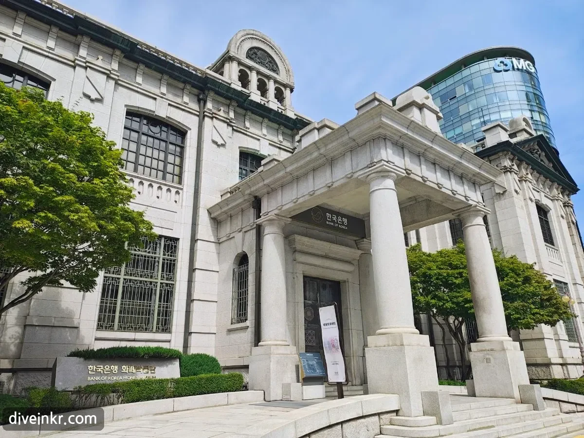 The granite Renaissance-style Bank of Korea Money Museum with a columned entrance portico, arched windows and a domed turret, a sign reading ํ๊ตญ์ํ BANK OF KOREA over the door and a stone marker reading ํ๊ตญ์ํ ํํ๋ฐ๋ฌผ๊ด BANK OF KOREA MONEY MUSEUM