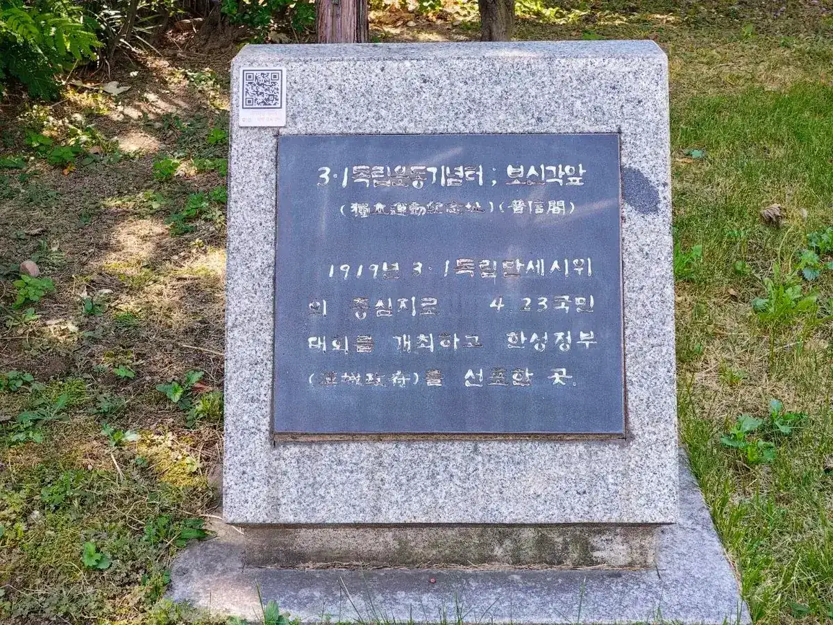 A granite memorial stone on the lawn in front of Bosingak with a dark metal plaque reading 3·1독립운동기념터 ; 보신각앞, followed by a short inscription in Korean with a few words in Chinese characters