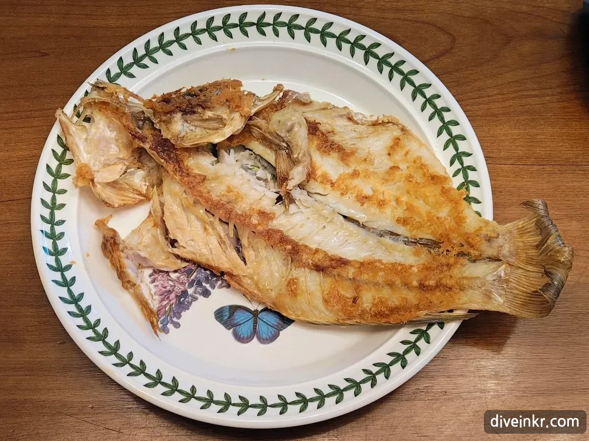 A whole white-fleshed fish, split open and grilled golden, on a round plate with a green leaf-pattern rim